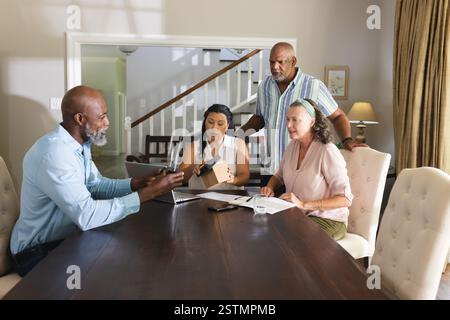 Diverse group discussing project at home, using laptop and documents on table. Collaboration, teamwork, brainstorming, planning, innovation, technolog Stock Photo