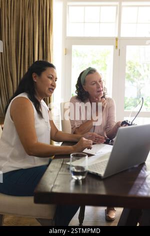 Senior women collaborating on laptop at home, discussing project with focus. Teamwork, collaboration, brainstorming, discussion, remote work Stock Photo