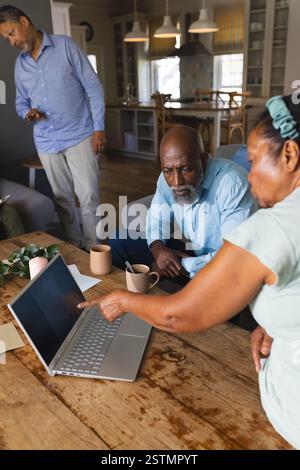 Seniors discussing project while using laptop at home, enjoying teamwork and coffee. collaboration, brainstorming, technology, discussion, housing, el Stock Photo