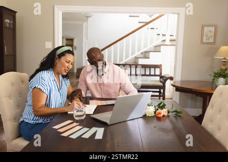 African American senior diverse couple planning home renovation using laptop at dining table. Home improvement, technology, teamwork, brainstorming, l Stock Photo