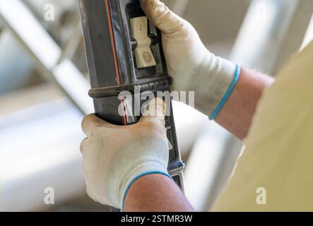 Worker operating a hoist crane control panel with protective gloves in an industrial setting Stock Photo