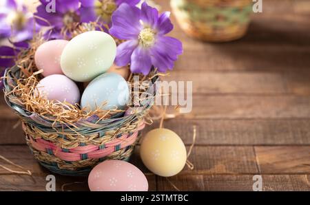 Pastel colored easter eggs in a basket and purple daisies on a rustic wooden table with copy space Stock Photo