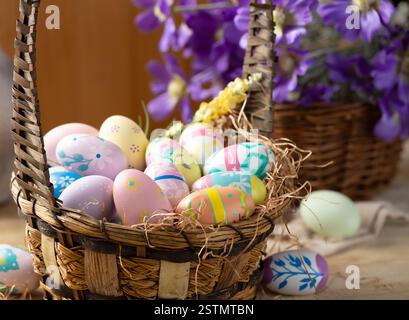 Decorated Easter eggs in a basket with purple daisies in background Stock Photo