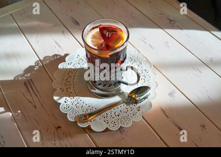 Non-alcoholic mulled wine served in vintage Soviet glass with traditional metal holder, garnished with lemon slice, star anise, on decorative white pa Stock Photo