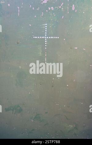 Illuminated perforations in a cross shape on a textured, weathered green metal surface, evoking industrial, architectural, or minimalist abstract desi Stock Photo