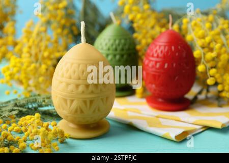 Colorful egg-shaped candles and mimosa flowers on turquoise wooden table, closeup. Easter decor Stock Photo