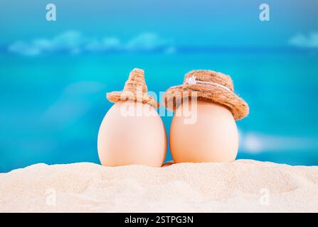 Happy easter. White eggs with hats on sandy beach of sea or ocean. Holiday postcard in hot country. Travel, spring, summer, vacations. Copy space Stock Photo