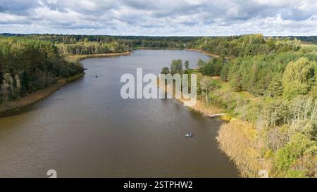 A serene aerial view of a river surrounded by lush green forests under a cloudy sky. Two small boats are visible on the water, indicating fishing or l Stock Photo