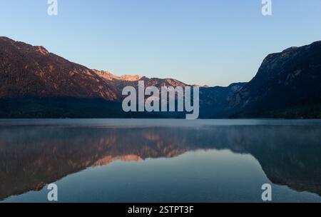 Lake Bohinj reflecting stunning golden sunrise with misty mountains on the background Stock Photo