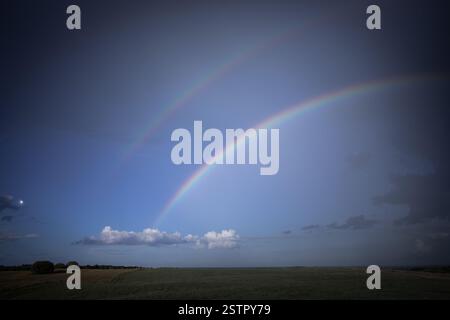 A mesmerizing double rainbow stretches across the sky over open fields, creating a surreal and serene natural scene. Stock Photo