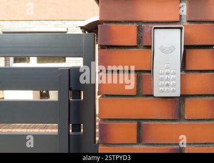 Modern Intercom Keypad on Brick Wall by Metal Gate Stock Photo