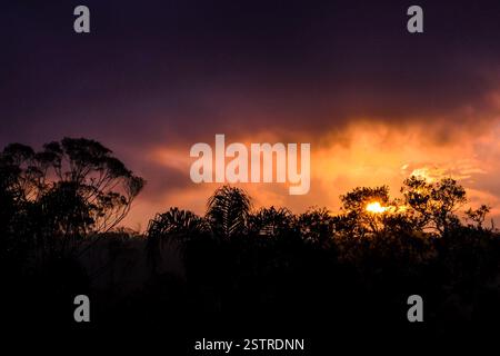 The image captures a stunning sunset with intense shades of orange and yellow contrasting against a dark, cloudy sky. The sun is partially hidden behi Stock Photo