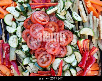 Vegetable platter before baking. Colorful, seasoned roasted vegetables with tomatoes, zucchini, eggplant, carrots, and bell peppers on a baking tray. Stock Photo