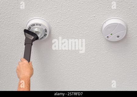 Person's hand vacuuming smoke and carbon monoxide detectors on a ceiling of a domestic room Stock Photo