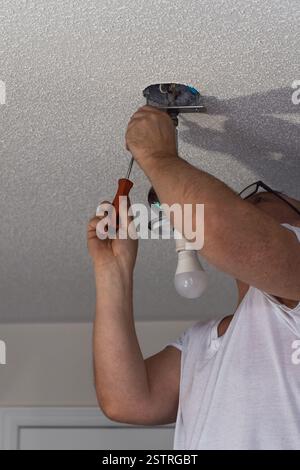 Middle aged man is replacing ceiling light fixture with using screwdriver Stock Photo