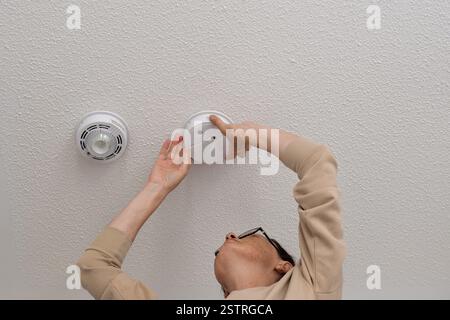 Woman reaching up for smoke alarm on ceiling at home Stock Photo