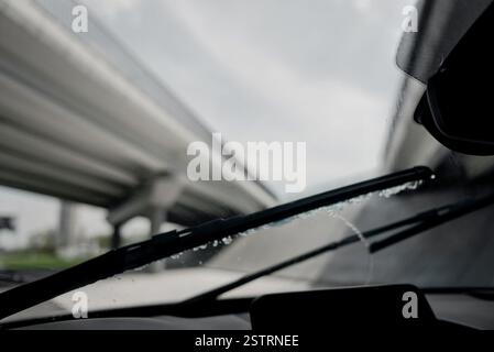 Windscreen wipers removing water from glass surface. Driver's point of view of driving a car in rain: windshield wipers working while car is driving. Stock Photo