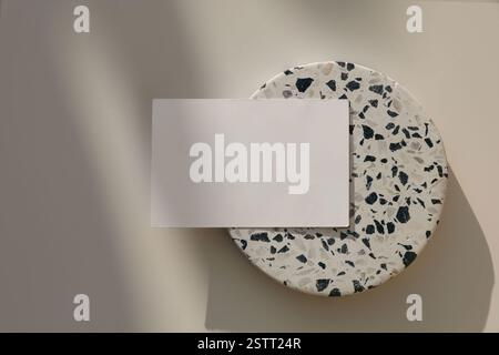 Blank horizontal greeting card, invitation mockup. Business card in sunlight. Black white round stone terrazzo tile, podium plate. Beige table Stock Photo