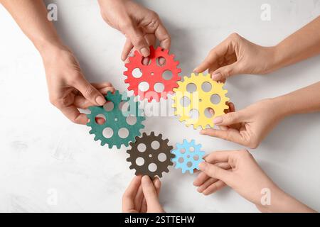 Hands holding wooden gears on light background, top view Stock Photo