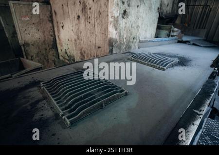 Two industrial grates sit atop a dusty dark surface in a factory setting Stock Photo