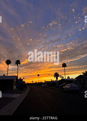 bright orange and indigo blue with spotty clouds above small arizona neighborhood in array of colors such as orange, red, purple, blue, and yellow Stock Photo