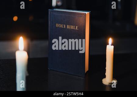 Holy Bible and two burning candles on the black table. The concept of faith and religion. christian faith. The inscription on the book translated from Stock Photo