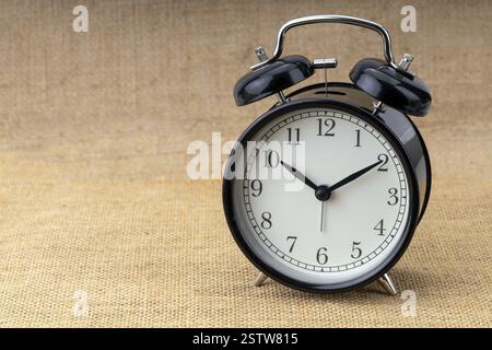 A classic retro alarm clock with a metal bell on brown background marking morning time. Stock Photo