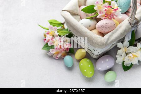 Colorful easter eggs and spring flowers overflowing from a white wicker basket on a light background Stock Photo