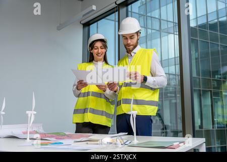 Two young engineers in yellow vests discussing new sustainability project Stock Photo
