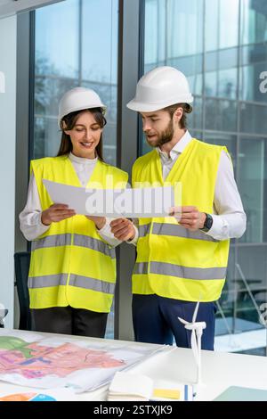 Two young engineers in yellow vests discussing new sustainability project Stock Photo