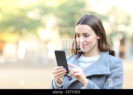 Satisfied female in winter using cell phone walking in the street Stock Photo