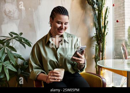 Smiling young woman sips coffee while browsing on her smartphone in a lively cafe. Stock Photo