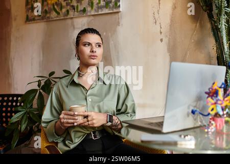 A young woman sips coffee at a cafe, focused on her laptop amid greenery. Stock Photo