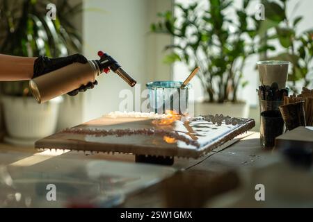 Palm of professional female artist works with burner, processing epoxy resin painting with fire. Stock Photo