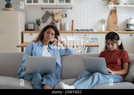 Modern family mother and daughter sit on sofa at home use digital devices laptops for work and study Stock Photo