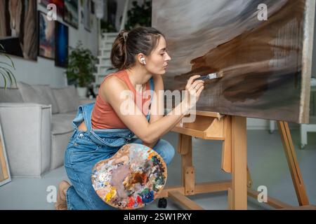 Professional female artist in light art studio painting picture. Portrait of creative woman painter. Stock Photo