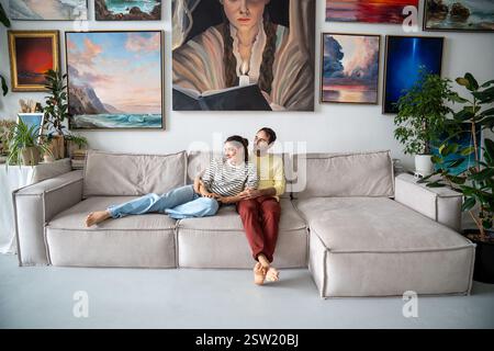 Happy relaxed loving couple rest on couch in home art gallery hugging dreaming looking aside window Stock Photo