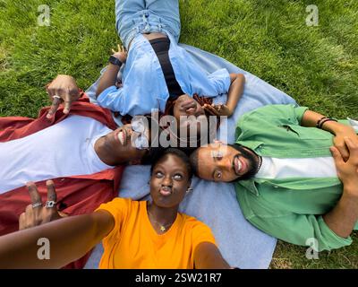 Group of four black students friends goofing around on grass in park, taking selfies while grimacing Stock Photo
