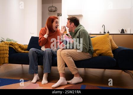Happy excited young married couple sitting with smartphone celebrating success Stock Photo