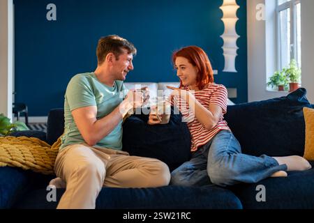 Happy relaxed couple drinking coffee or tea while resting together at home, enjoying weekend morning Stock Photo