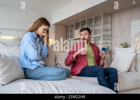 Family in argument on sofa, woman cries and suspects husband of unfaithfulness. Marital discord Stock Photo