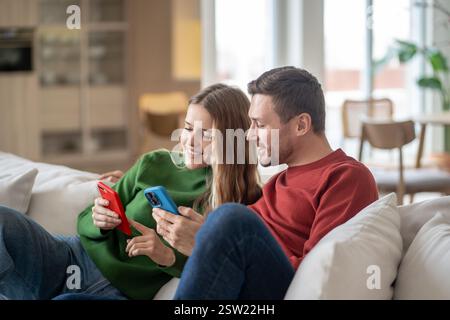 Loving couple sitting on sofa, looking photos, videos in internet, spending pastime together at home Stock Photo