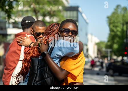 Joyful black students in good mood hugging each other in friendly warmly way on street outside. Stock Photo
