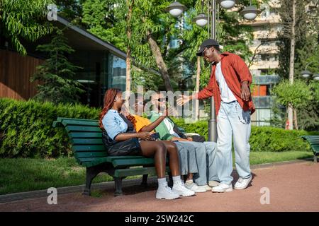 Pleasant meeting of calm relaxed African American students friends in park, sitting on alley bench Stock Photo