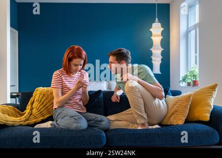Unhappy young couple arguing while sitting on couch home. Nervous tyrant husband humiliates wife Stock Photo
