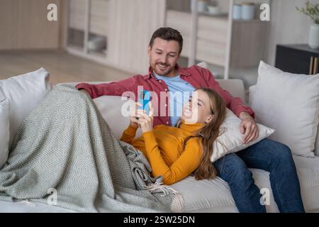 Cheerful married couple spending fun quiet time together resting on sofa watching online content. Stock Photo