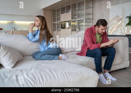 Sad unhappy married couple in quarrel sitting on sofa couch in living room ignoring each other. Stock Photo