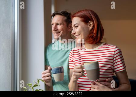 Smiling happy couple drinking coffee looking out window Stock Photo