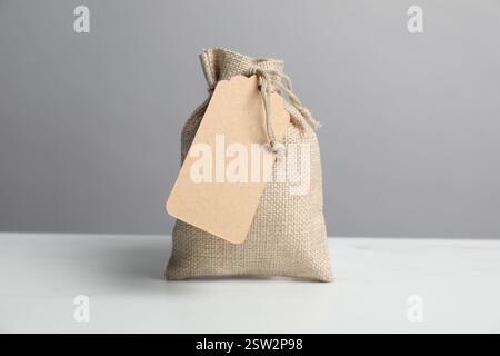 One burlap bag with tag on white table against grey background Stock Photo