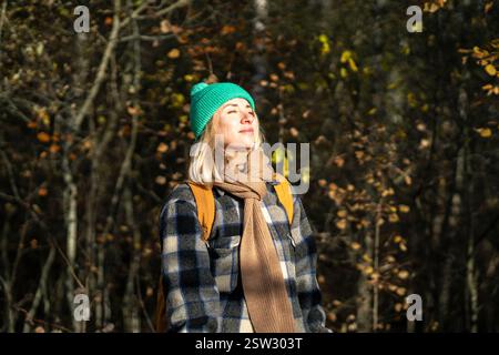 Pleased Scandinavian middle aged woman enjoys stroll in autumn forest park smiling looking to sun Stock Photo